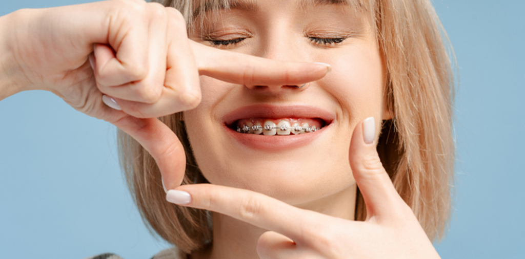 a girl framing her smile with braces in front of a blue background